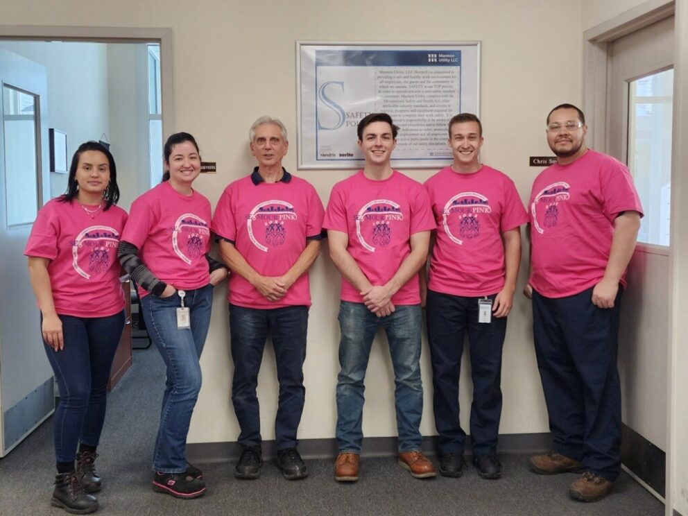 Workers wearing pink t-shirts gathered in an office in front of safety signage